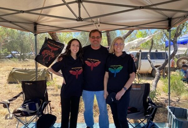 Milliya Rumurra Aboriginal Corporation CEO Andrew Amor with WANADA’s Rochelle McIntosh and Helin Cimen under the shade of a tarp, smiling on a bright sunny day.