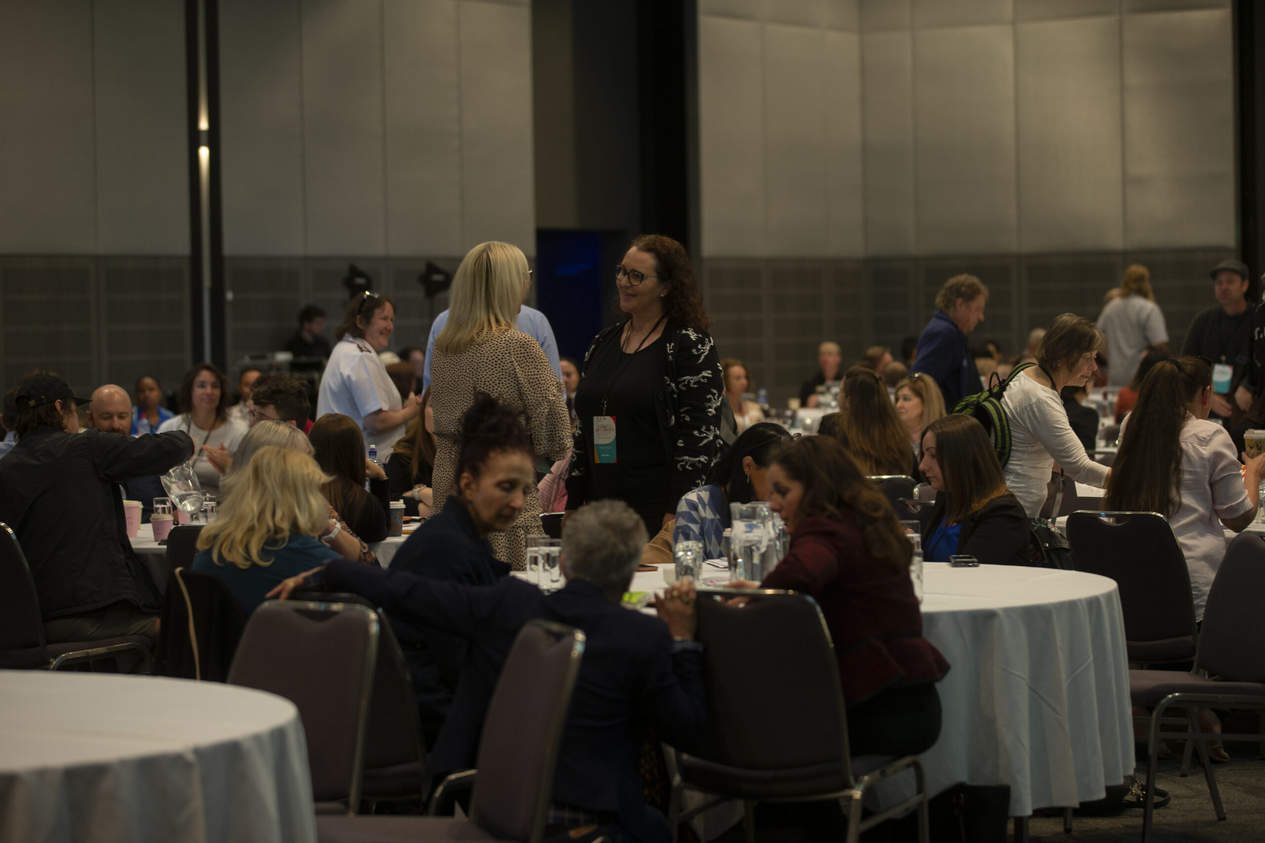 People sitting and standing in a conference room with round tables.