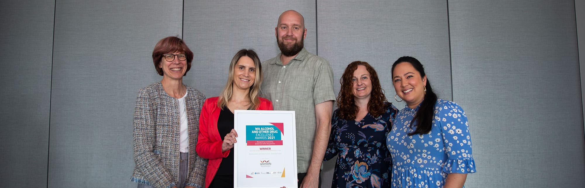 Four women and a tall man standing while one of the women holds a large certificate.