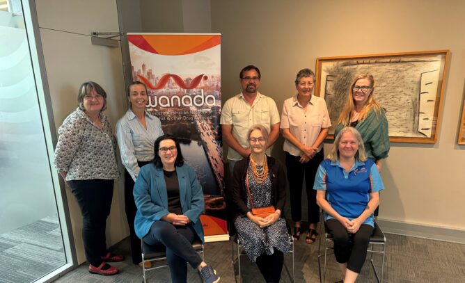 Four women and a man standing in front of a WANADA banner and behind three women sitting indoors.