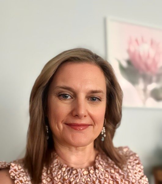 Headshot of a smiling woman in a brown and white top