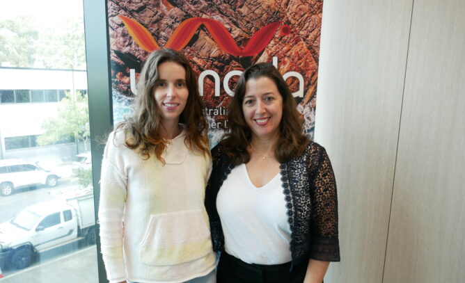 Two women, Amie Furlong and Ganit-Poleg Spark standing in front of a WANADA banner and next to a window, smiling.